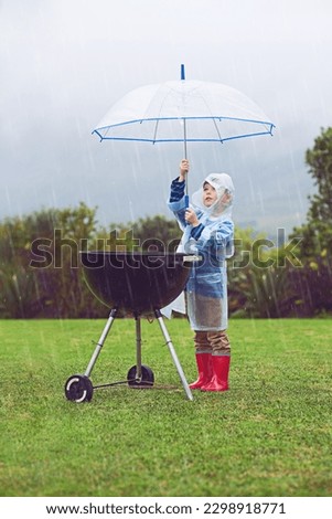 Rain, umbrella and a boy covering a barbecue outdoor on a field while cooking food alone in winter. Raincoat, kids and insurance with a young male child trying to protect a bbq during stormy weather