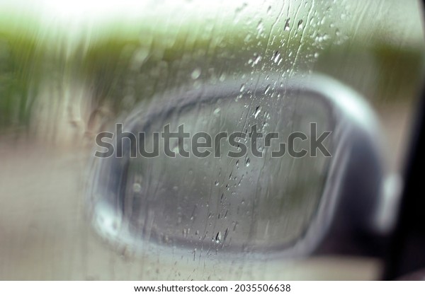 Rain water droplets on a window with trees \
cars and people behind the blurred\
glass