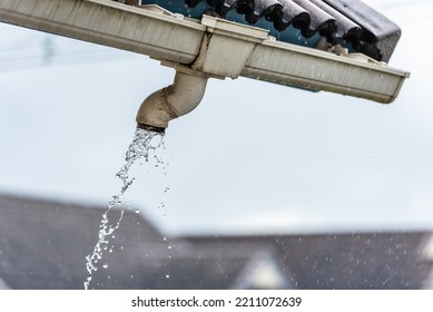 Rain water flowing down from old plastic roof gutter in rainy day.