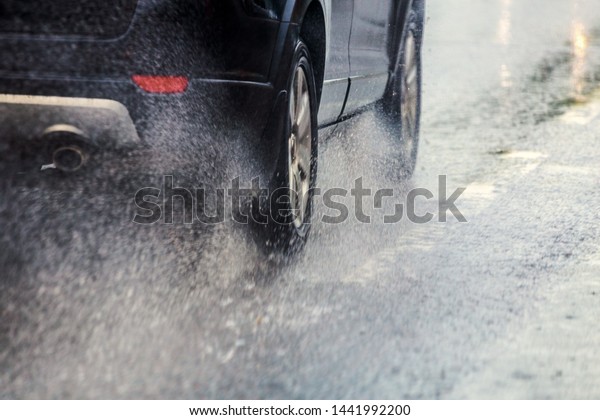 rain water splash flow from\
wheels of black car moving fast in daylight city with selective\
focus