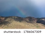 A rainbow appears behind a mountain range in the desert. 
