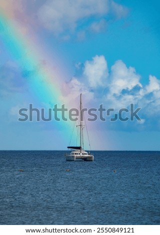 Rainbow appears on a cloudy blue sky afrer rain. Rainbow crosses sailors on a sailing boat in the ocean in Gran Canaria. Beautiful background with a boat and rainbow.