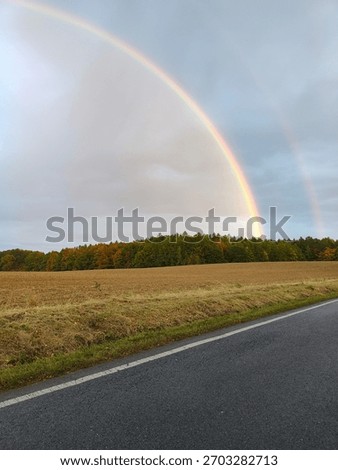 A rainbow arching over a field and road