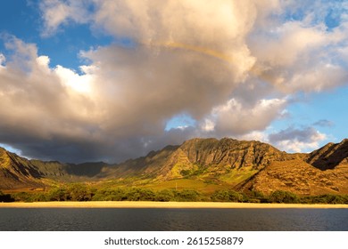 A rainbow arcs over the dramatic mountain ranges of Oahu, Hawaii at sunset.