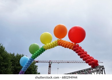 Rainbow Balloon Arch Against Cloudy Sky And Cranes