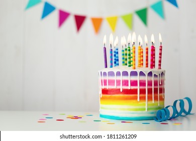 Rainbow birthday cake with colorful candles and drip icing