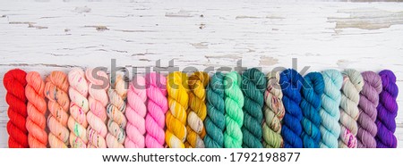 A rainbow border of yarn on a weathered white wood tabletop
