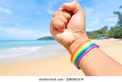 ็Hand In A Rainbow Bracelet. Festival People Celebrate Meting  LGBTQ+ Gay Pride Month Event Day Concept 2022. Colorful Rainbow Gender Symbol Heart Sex Love Flag Background United Kingdom. Lesbian.