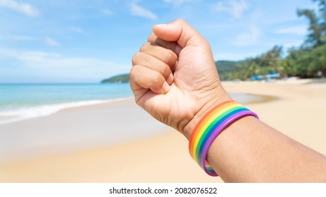 ็Hand In A Rainbow Bracelet. Festival People Celebrate Meting  LGBTQ+ Gay Pride Month Event Day Concept 2022. Colorful Rainbow Gender Symbol Heart Sex Love Flag Background United Kingdom. Lesbian.