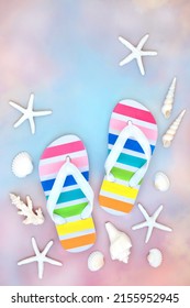 Rainbow colored flip flops, off on holiday abstract concept with sea shells on pastel pink and blue gradient sky background. Vacation, travel destinations and LGBT composition.