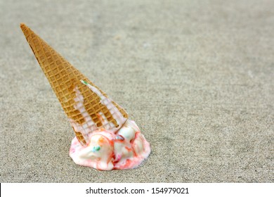 A rainbow colored ice cream cone has dropped upside down on the sidewalk on a summer day