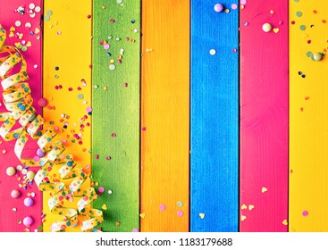 Rainbow Colored Wood Carnival Background With Coiled Streamers, Scattered Confetti And Sugared Candy Around Central Blank Copy Space