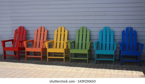 Rainbow Colors Of  Adirondack Chairs In A Row Outside.  