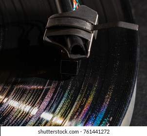 Rainbow colors from grooves in long playing vinyl record with old fashioned tonearm and cartridge in the tracks