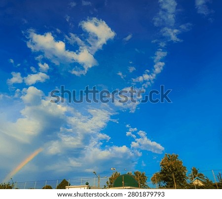 Rainbow crosses bright clouds during the day under beautiful buildings