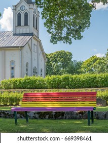 Rainbow Flag Colors On Bench, Church In Background. Gay Marriage Concept.