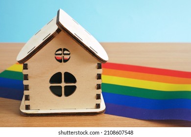 Rainbow Flag As LGBT Gay Symbol And Model Of House On Wooden Background, LGBT+ Family Concept, Closeup