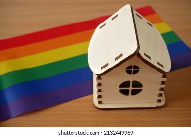 Rainbow Flag As LGBT Gay Symbol And Model Of House On Wooden Background, LGBT+ Family Concept, Closeup