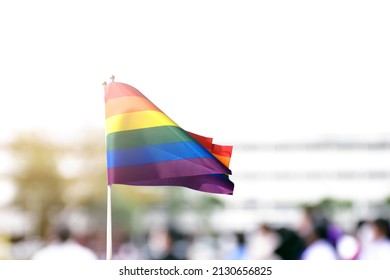 Rainbow Flag, A Symbol For The LGBT Community, Waving In The Wind With Blur Asian Students In The Morning Activities Background. Concept For Supporting And Campaigning The Lgbtq+ Communities At School