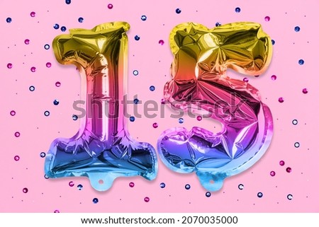 Rainbow foil balloon number, digit fifteen on a pink background with sequins. Birthday greeting card with inscription 15. Anniversary concept. Top view. Numerical digit. Celebration event, template.