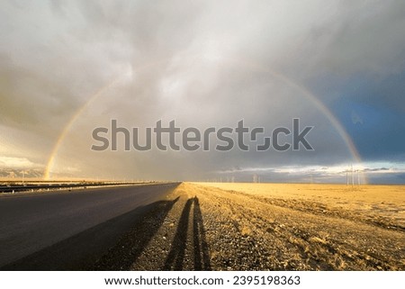 Rainbow forming an arch over a road on a sunny morning with dramatic cloudy skies.