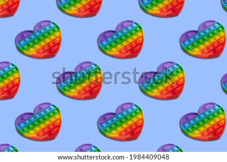 Rainbow heart shape isometric pattern of silicon toy for kids. Pop it fidget toy on pastel background. Simle dimple toy on blue pastel background. 