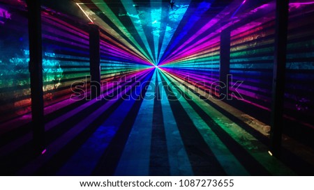 Rainbow laser beams shine from a central point past four silhouetted columns on an otherwise empty background. Music festival / nightclub / heaven 