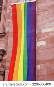 Rainbow LGBT Flag Handing Down By The Catholic Church Of The Holy Spirit In The Center Of Heidelberg, Germany. Brick Wall On The Background