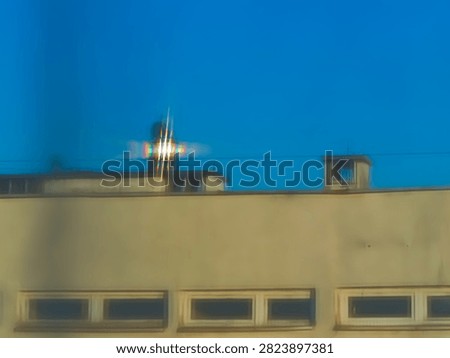 Rainbow light diffraction created by sunlight passing through a sheer curtain, producing spectral colors and a starburst effect over an urban building and blue sky