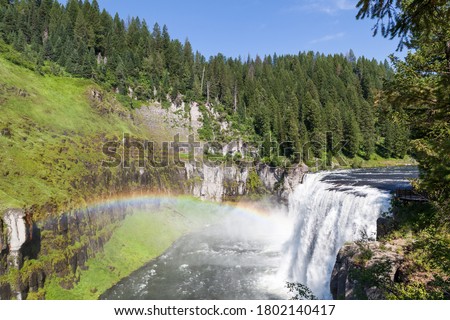 A rainbow in the mist of Upper Mesa Falls as it cascades over a cliff in the rugged wilderness of Henrys Fork of the Snake River along the Mesa Falls Scenic Byway in Idaho.