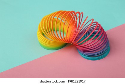 Rainbow plastic multicolored spiral slinky toy on pink blue background