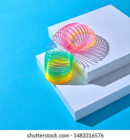 Die mehrfarbige Rainbow-Plastik-Federspirale geht eine weiße Treppe hinunter, Schritt für Schritt auf pastellfarbenem Hintergrund mit Schatten, Kopienraum.
