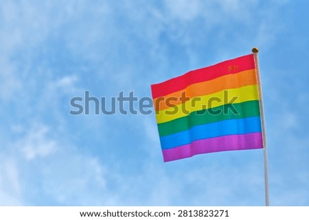 Rainbow Pride Flag on Blue Sky Background. Minimal composition featuring a rainbow Pride flag positioned beside a large open area for text or graphic elements. Commercial image suitable for awareness campaigns, websites, presentations, publications, and advertising materials.