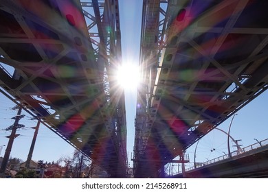 The rainbow rays of the sun shine on the railway bridge. On the left are power lines, on the right is a road bridge. - Powered by Shutterstock