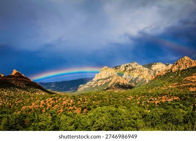 A rainbow is seen over a mountain range. The sky is cloudy and the mountains are covered in trees