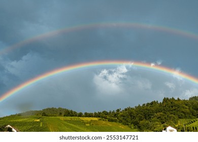 A rainbow is seen in the sky above a hillside. The sky is cloudy and the sun is not visible