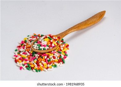 Rainbow Sprinkles In Wooden Spoon On A Pile Of  Rainbow Sprinkles On White Background With Clipping Path.