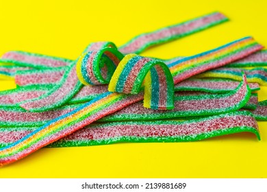 Rainbow Stripes Of Sour Jelly Candies In Sugar Sprinkles On A Yellow Background. Top View. Colorful Jelly Candies In Sugar Sprinkles. Rainbow Candy Background. Selective Focus. 