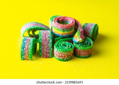 Rainbow Stripes Of Sour Jelly Candies In Sugar Sprinkles On A Yellow Background. Top View. Colorful Jelly Candies In Sugar Sprinkles. Rainbow Candy Background. Selective Focus. 