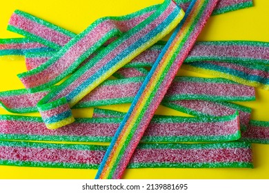 Rainbow Stripes Of Sour Jelly Candies In Sugar Sprinkles On A Yellow Background. Top View. Colorful Jelly Candies In Sugar Sprinkles. Rainbow Candy Background. Selective Focus. 