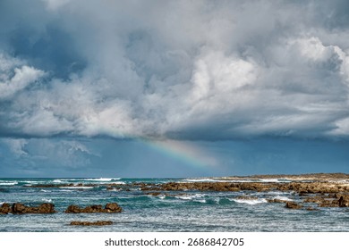 A rainbow through the clouds over the ocean of Struisbaai