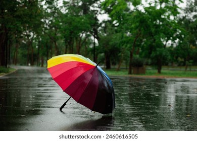 A rainbow umbrella is open in the rain. The umbrella is colorful and has a rainbow pattern. The rain is falling, and the umbrella is protecting the person underneath it. The scene is peaceful - Powered by Shutterstock