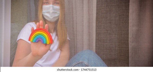 Rainbow In The Window. Thank You NHS, Promotion In Support Of Doctors In The Coronavirus Pandemic, Covid 19. Family In The Window Of The House In Masks And A Rainbow In Hands. National Health System