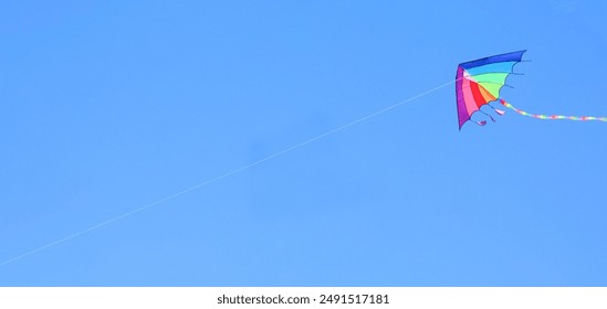 rainbow-colored kite soars through the clear blue sky attached to a string held by someone below