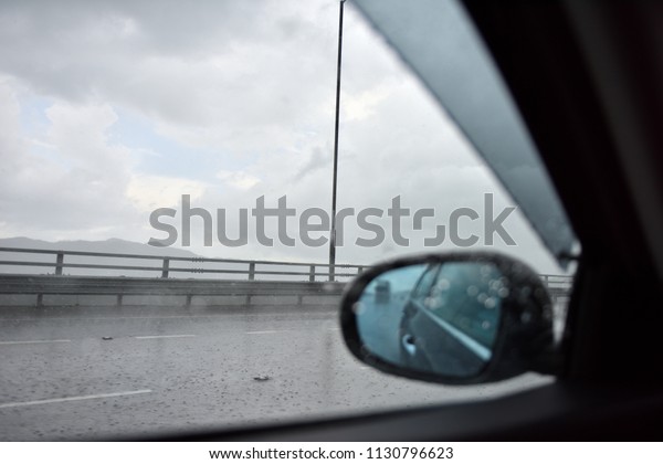 Raindrop on a side mirror and a side window while\
a car is running on the slippery road crossing a bay bridge with\
clear sky during a raining\
season.