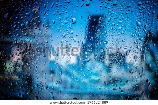 Raindrop on\
the window, backgorund is bluried a light of city. City life in\
night in rainy season abstract\
background.
