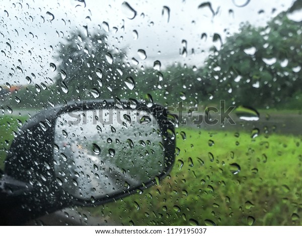 Raindrop outside the car in raining day on street\
with blurred green grass side way. Good view from driver\
seat.Selective focus.