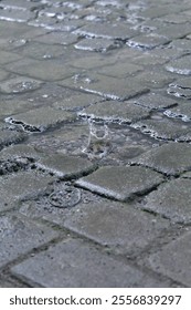 Raindrops causing a puddle on a road made of paving blocks