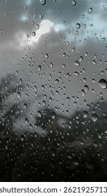 Las gotas de lluvia se aferran a la ventanilla de un automóvil, difuminando la vista de un cielo nublado y árboles distantes, creando una atmósfera tranquila y malhumorada. La luz Filtrar suavemente a través de las gotitas, añadiendo un efecto de ensueño.

