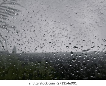 Raindrops cling to a window pane, blurring a lush, grey landscape outside. Perfect for conveying a cozy, melancholic atmosphere.